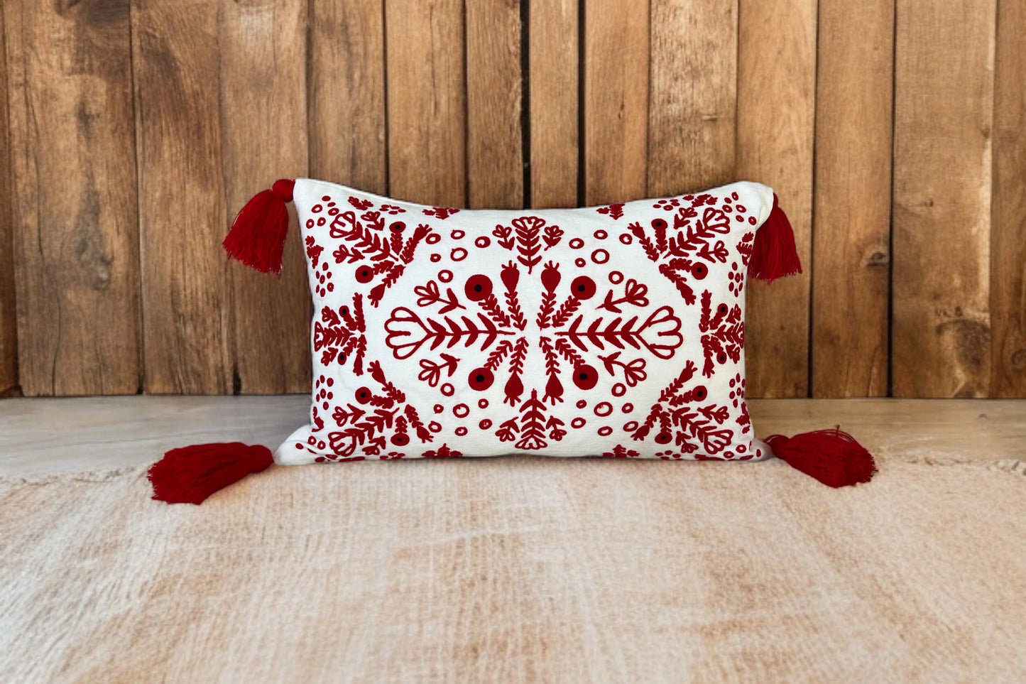Red and white embroidered boho pillow with tassels placed on a brown jute rug