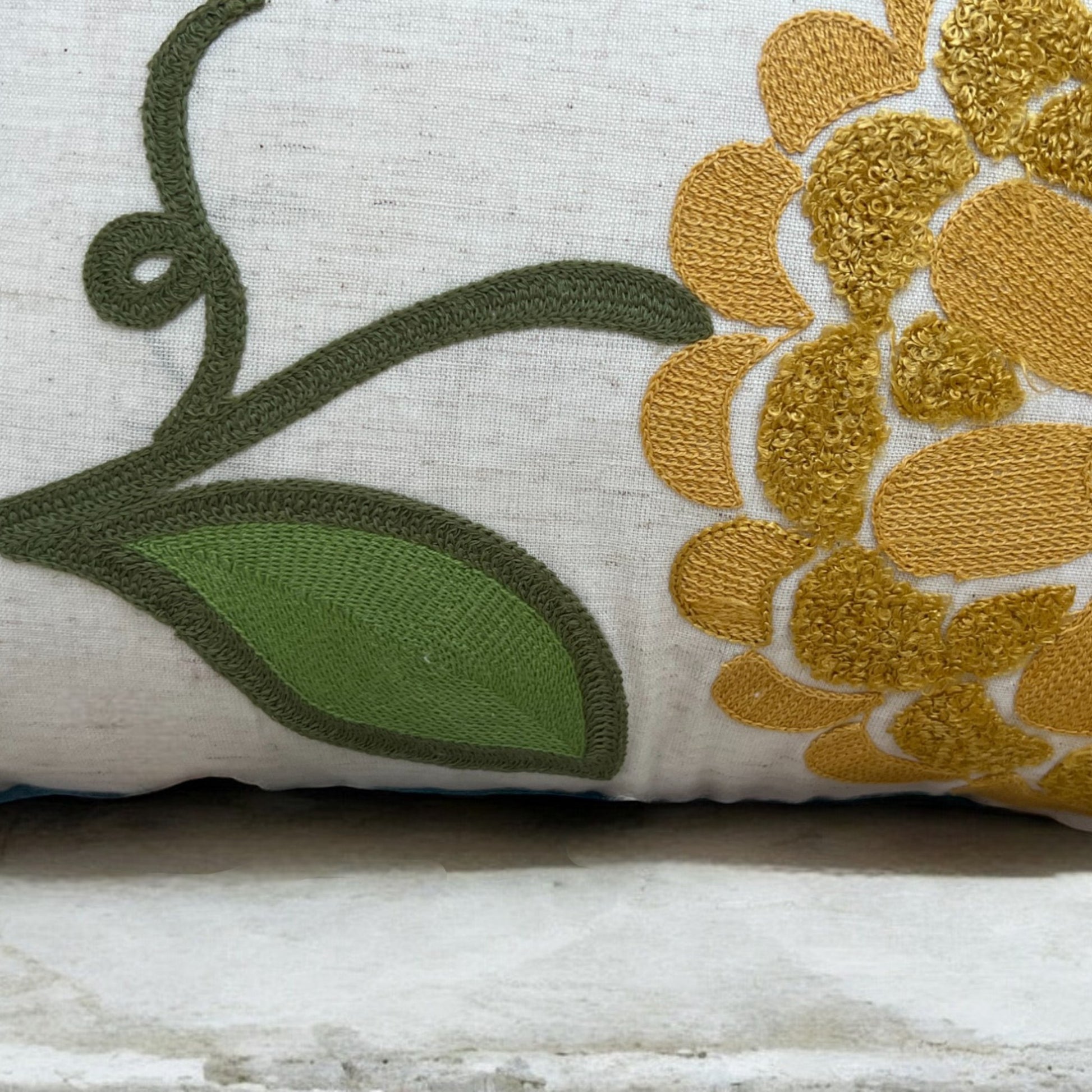 Decorative pillow with embroidered gold flower and green leaves on a white background