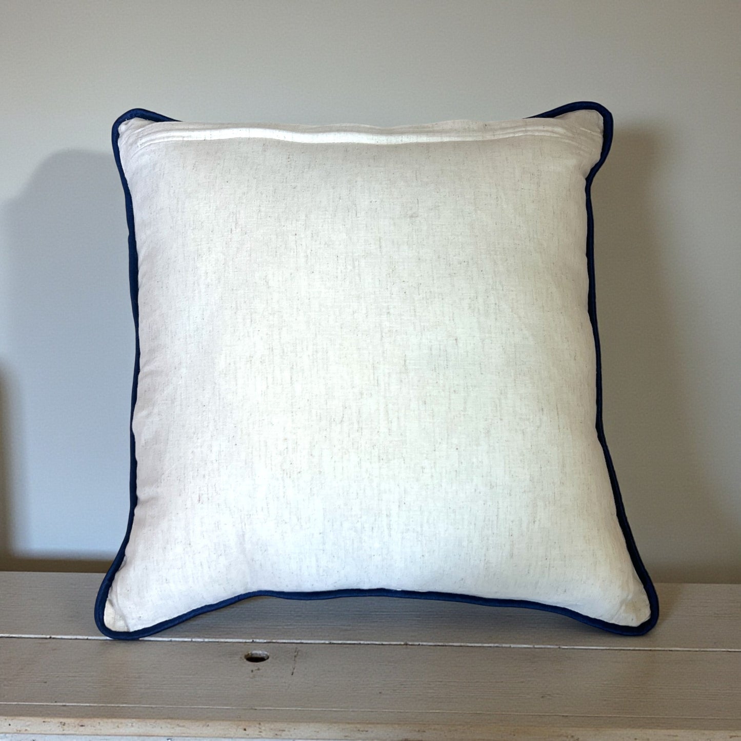 White pillow with navy blue trim on a wooden surface
