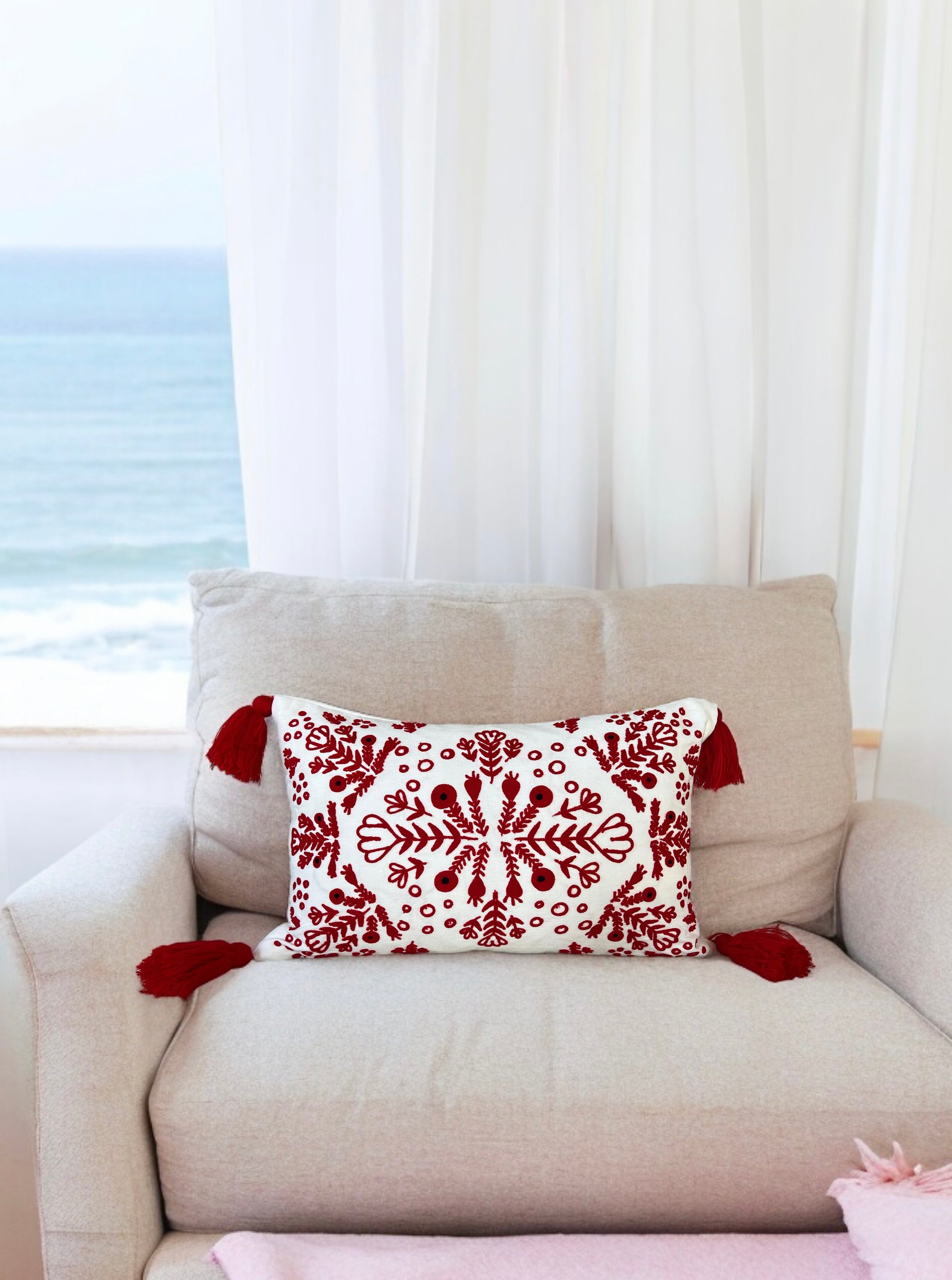 Red and white embroidered boho pillow with tassels placed on a cream armchair