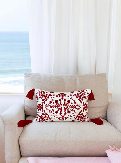 Red and white embroidered boho pillow with tassels placed on a cream armchair